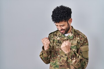 Wall Mural - Arab man wearing camouflage army uniform very happy and excited doing winner gesture with arms raised, smiling and screaming for success. celebration concept.