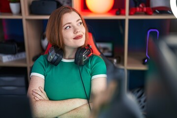 Poster - Young redhead woman streamer smiling confident sitting with arms crossed gesture at gaming room