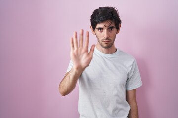 Poster - Young hispanic man standing over pink background doing stop sing with palm of the hand. warning expression with negative and serious gesture on the face.