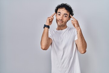 Wall Mural - Hispanic man standing over isolated background smiling pointing to head with both hands finger, great idea or thought, good memory