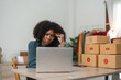 © Natee Meepian - Stressed young entrepreneur African American woman and courier parcel box at home office. Small business owner, online market delivery, lifestyle freelance concept