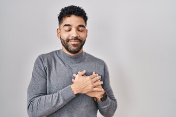 Poster - Hispanic man with beard standing over white background smiling with hands on chest with closed eyes and grateful gesture on face. health concept.