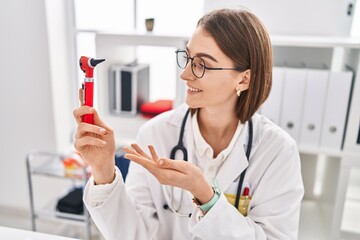 Poster - Young caucasian woman doctor holding otoscope at clinic