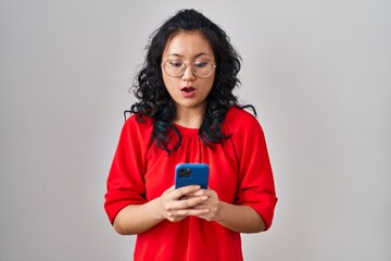 Wall Mural - Young asian woman using smartphone typing message afraid and shocked with surprise and amazed expression, fear and excited face.