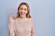 © Krakenimages.com - Hispanic woman standing over blue background smiling positive doing ok sign with hand and fingers. successful expression.