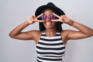 Canvas Print - Young african american with braids wearing hat and sunglasses doing peace symbol with fingers over face, smiling cheerful showing victory