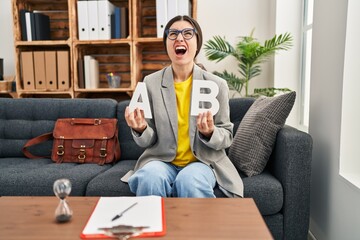 Poster - Young hispanic woman working at consultation office angry and mad screaming frustrated and furious, shouting with anger looking up.