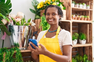 Poster - Middle age african american woman florist smiling confident using smartphone at flower shop