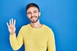 © Krakenimages.com - Hispanic man standing over blue background showing and pointing up with fingers number four while smiling confident and happy.