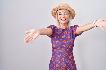 Sticker - Young caucasian woman wearing flowers dress and summer hat looking at the camera smiling with open arms for hug. cheerful expression embracing happiness.