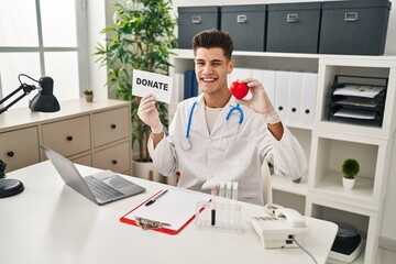 Wall Mural - Young hispanic doctor man supporting organs donations winking looking at the camera with sexy expression, cheerful and happy face.