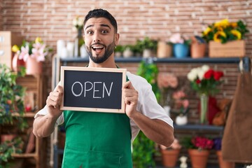 Wall Mural - Hispanic young man working at florist holding open sign celebrating crazy and amazed for success with open eyes screaming excited.