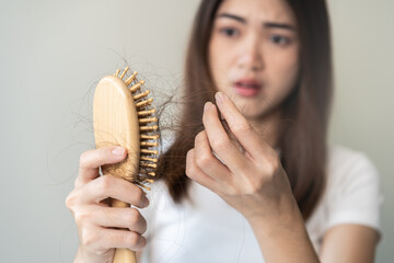 Serious asian young woman holding brush holding comb, hairbrush with fall black hair from scalp after brushing, looking on hand worry about balding. Health care, beauty treatment, hair loss problem.