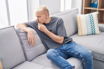 Wall Mural - Young caucasian man sitting on sofa with serious expression at home