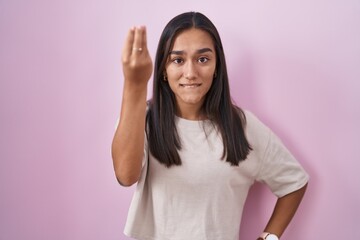 Wall Mural - Young hispanic woman standing over pink background doing italian gesture with hand and fingers confident expression