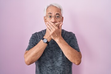 Poster - Middle age man with grey hair standing over pink background shocked covering mouth with hands for mistake. secret concept.