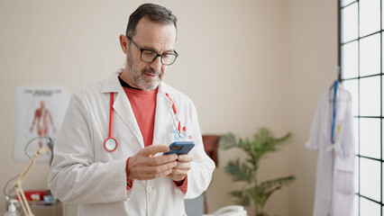 Wall Mural - Middle age man doctor smiling confident using smartphone at clinic