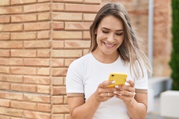 Wall Mural - Young caucasian woman smiling confident using smartphone at street