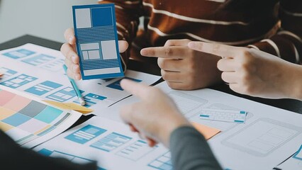 Close up ux developer and ui designer brainstorming about mobile app interface wireframe design on table with customer breif and color code at modern office.Creative digital development agency