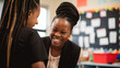 © Wild Awake - Diversity and Minority Representation in Education: Smiling Black BIPOC, Female Teacher Helping a Student in the Classroom. African American Educator Helping a Young Student in Classroom Generative Ai
