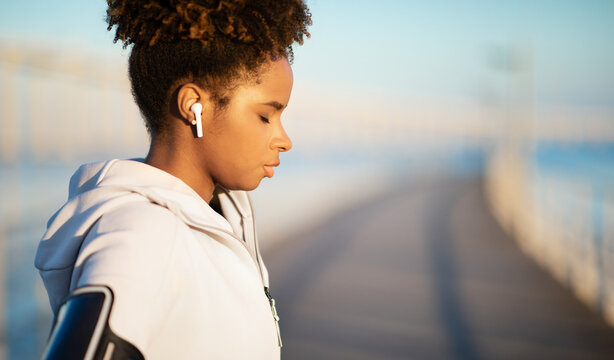 Wall Mural - Young Black Female Wearing Wireless Earphones Standing With Closed Eyes Outdoors