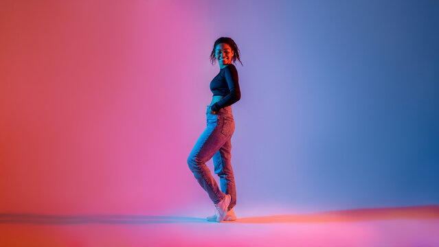 Wall Mural - Full length of stylish african american woman posing in neon light in studio and smiling at camera