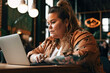 © Nedrofly - Body positive plus size woman using laptop in coffee shop