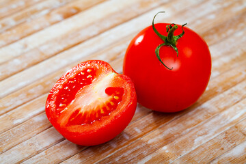 Wall Mural - Two fresh juicy red tomatoes placed on wooden table. One cutted in half.