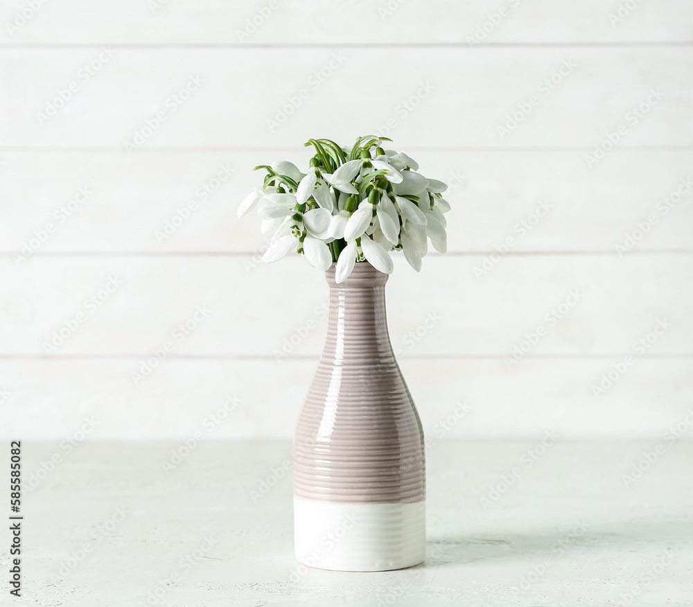Vase with beautiful snowdrops on white wooden background