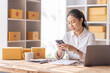© David - Asian SME business woman using laptop computer Phone checking customer order online shipping boxes at home. Starting Small business entrepreneur SME freelance. Online business, Work at home concept.