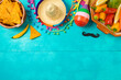 Cinco de Mayo holiday celebration with nacho chips, peppers, maracas and mexican party decorations on blue wooden background. Top view, flat lay