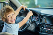 © Aleksandr - Happy boy is holding onto the steering wheel of the car, smiling broadly with joy. Smiling child in a modern car sits in the driver's seat, dreaming of winning a real race
