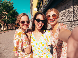 Wall Mural - Three young beautiful smiling hipster female in trendy summer dresses clothes. Sexy carefree women posing in the street. Positive models having fun, talking, chatting. Going crazy. Taking selfie