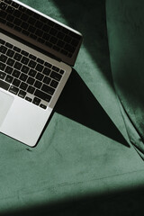 Wall Mural - flatlay laptop computer on green velour sofa with aesthetic sunlight shadows. minimal work, business