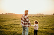 © La Famiglia - Happy family on holiday vacation. Smiling father and little daughter holding hands and walking together on the meadow field. Parent with child girl relax and enjoy an outdoor lifestyle. Copy space