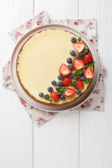 Wall Mural - Classic Freshly New York Cheesecake with fresh berries and mint closeup on the plate on the wooden table. Vertical top view from above