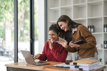 Wall Mural - Two diverse female smiling while working together at a boardroom table during a meeting in a modern office