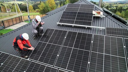 Wall Mural - Technicians installing photovoltaic solar panels on roof of house. Drone view of men engineers in helmets building solar module system with help of hex key. Concept of alternative, renewable energy.