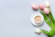 Spring background with flowers, a cup of coffee and a bouquet of pink and white tulips on colored table background with place for text. Copy space top view