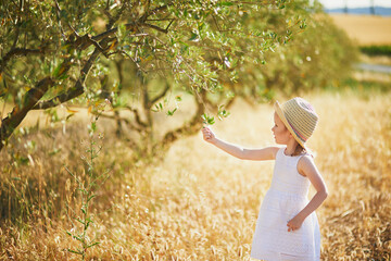 Adorable 4 year old girl in white dress and straw hat near olive tree, Provence, France