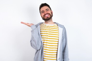 Wall Mural - Young caucasian mán wearing trendy clothes over white background smiling cheerful presenting and pointing with palm of hand looking at the camera.