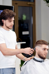 Wall Mural - Barber trim hair with clipper on handsome bearded man