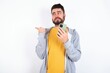 © Jihan - Young caucasian mán wearing trendy clothes over white background points thumb away and shows blank space aside, holds mobile phone for sending text messages.