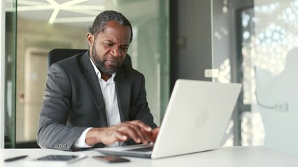 Frustrated man complaining about poor performance of computer program on laptop while sitting in modern office. Angry businessman is dissatisfied with the work of a computer, the Internet or service