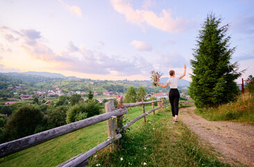 Wall Mural - Young woman enjoying the mountains view on the green meadaw walking by pathway.