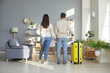 © Studio Romantic - Romantic couple is back home from summer holiday trip. Back view of young man and woman who have just returned from vacation travel with yellow suitcase standing in living room and holding hands