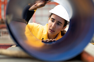 Wall Mural - Industrial Engineer wears safety helmet work in heavy metal engineering factory. Young female industry worker in hard hat checking production machinery equipment in metalwork manufacturing facility.