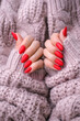 Women's hands with a beautiful matte oval manicure in a warm pink knitted sweater. Winter trend, cover red nails with gel polish, shellac.