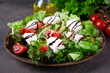Salad with mozzarella cheese, lettuce, cucumber and tomatoes with spices and olive oil topped with balsamic glaze on brown plate