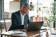 © standret - Using laptop. Senior businessman is working in the office